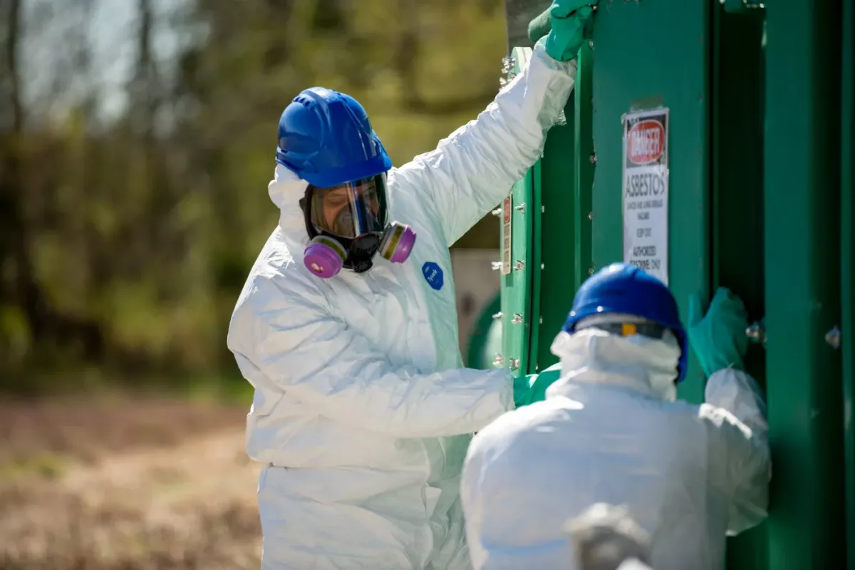 Asbestos inspector in protective gear collecting a bulk sample of ceiling material for lab analysis